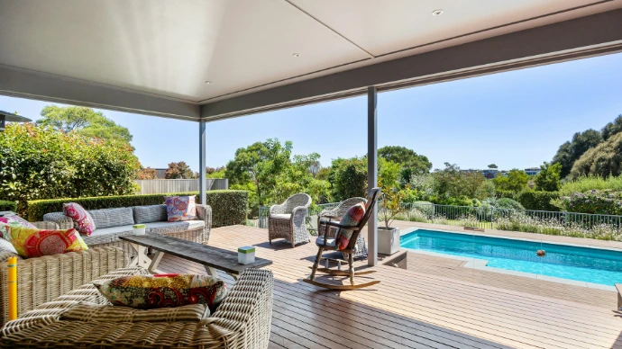 A covered deck with a couch and a table with a bowl of fruit on it